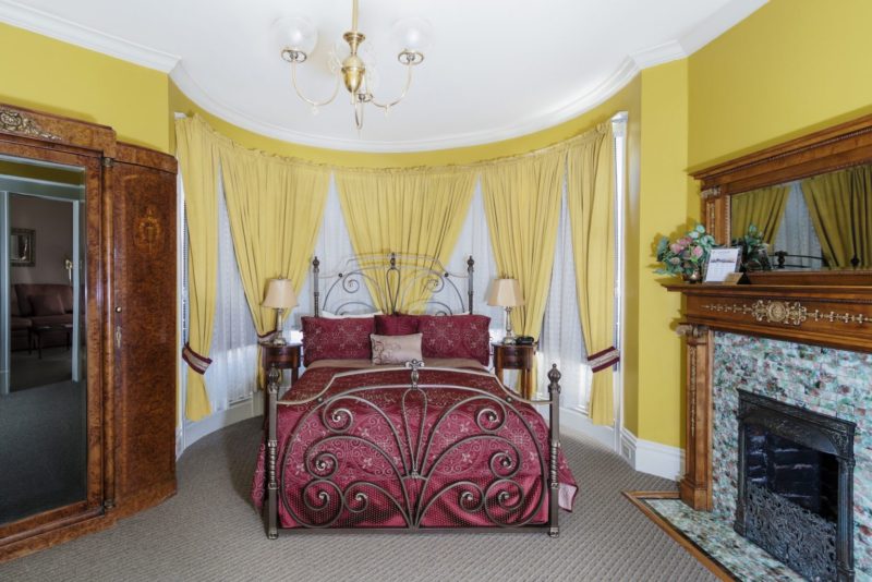 Photo of bedroom with yellow walls, queen bed and tile-faced decorative fireplace